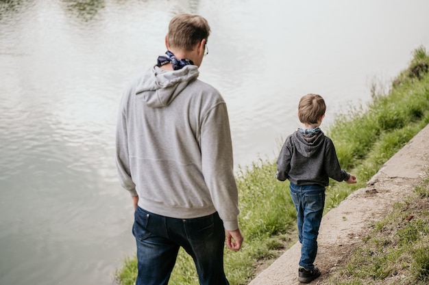 Padre e hijo caminando por la orilla del río vista trasera
