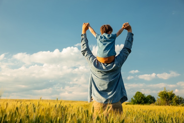 Foto padre e hijo en el campo de trigo, niño sentado sobre los hombros de su padre