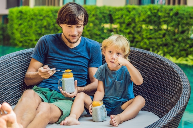 Padre e hijo comen postre con semillas de chía y mangos junto a la piscina por la mañana. alimentación saludable, comida vegetariana, dieta y concepto de personas