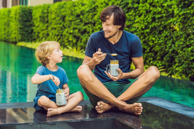 Padre e hijo comen postre con semillas de chía y mangos junto a la piscina por la mañana. concepto de alimentación, comida vegetariana, dieta y personas saludables.