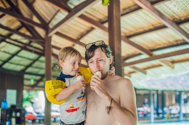 Padre e hijo comiendo helado en un parque acuático bajo un techo de paja