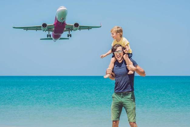 Padre e hijo se divierten en la playa viendo el aterrizaje de aviones. Viajar en avión con concepto de niños.