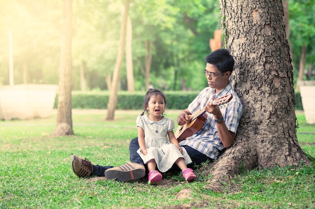 Padre e hijo se divierten tocar la guitarra juntos en el parque