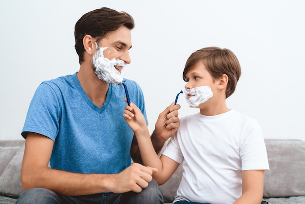 Padre e hijo con espuma en las caras se afeitan entre sí.