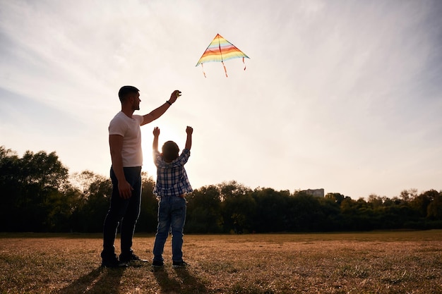 Padre e hijo están con cometa en el campo iluminado por la luz del sol
