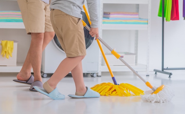 Padre e hijo están limpiando el piso de la casa juntos usando mp amarillo plano cerrado con caras no reconocibles en una colorida habitación.