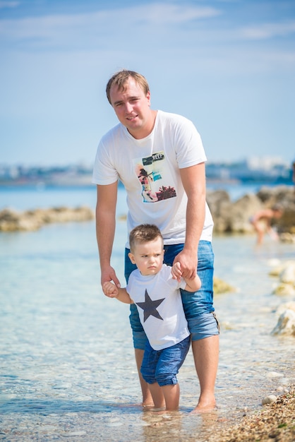 Padre e hijo de familia feliz de pie sobre un pontón de madera frente al mar en verano.