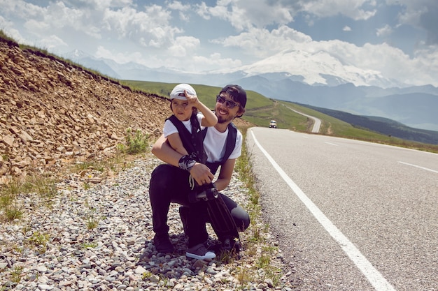 Padre e hijo con gorras y gafas de sol cogen un coche parado en la carretera en las montañas