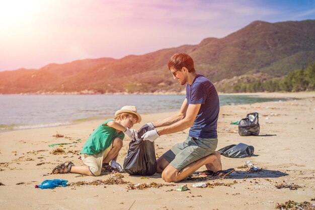 Foto padre e hijo con guantes limpiando la playa recogiendo bolsas de plástico que contaminan el mar educación natural