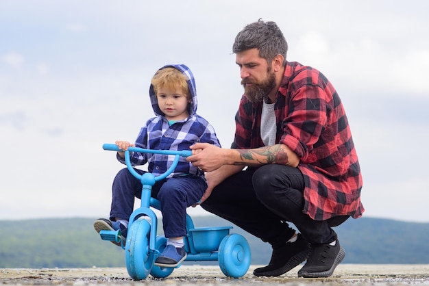 Padre e hijo juegan con la bicicleta al aire libre, un niño pequeño aprendiendo a andar en bicicleta con su papá f