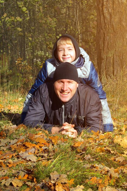 Padre e hijo juegan en el bosque otoñal.Un adolescente de apariencia europea se ríe con su padre.