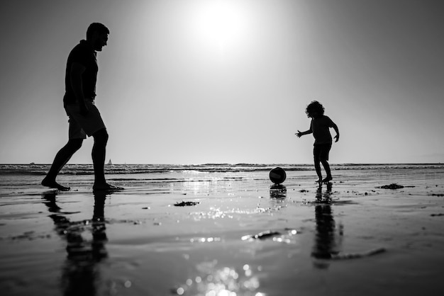 Padre e hijo juegan fútbol o fútbol en la playa papá con niño niño en un día de verano