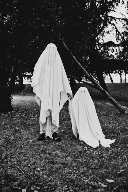 Foto padre e hijo jugando fantasmas con sábanas blancas en el jardín, fotos conceptuales sobre las fiestas de halloween