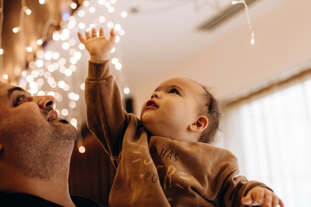 Foto padre e hijo jugando con luces guirnaldas padre sostiene a su bebé en los brazos etnia turca