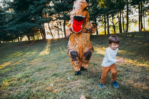 Padre e hijo jugando en el parque, con un disfraz de dinosaurio, divirtiéndose con la familia al aire libre