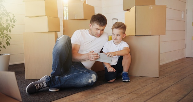 Padre e hijo jugando con tableta digital rodeada de cajas