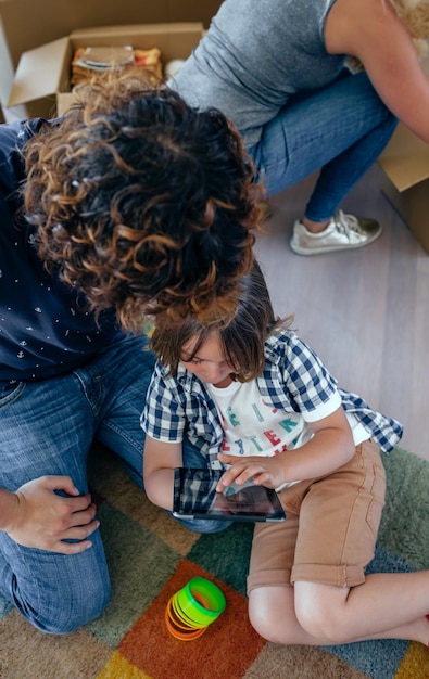 Foto padre e hijo jugando a la tableta mientras la madre desempaca cajas de mudanza