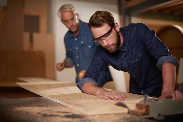 Padre e hijo de madera en un taller arquitecto y carpintero con renovación o gafas de seguridad con protección Hombres padres o trabajo en equipo con construcción o construcción con planificación para proyecto o equipo