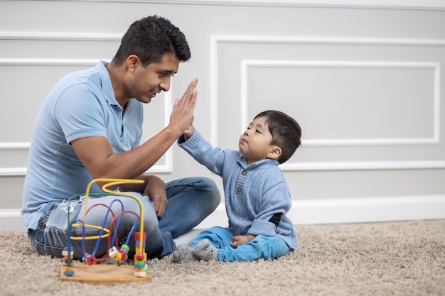 Padre e hijo mexicano jugando en la alfombra en casa, choca esos cinco