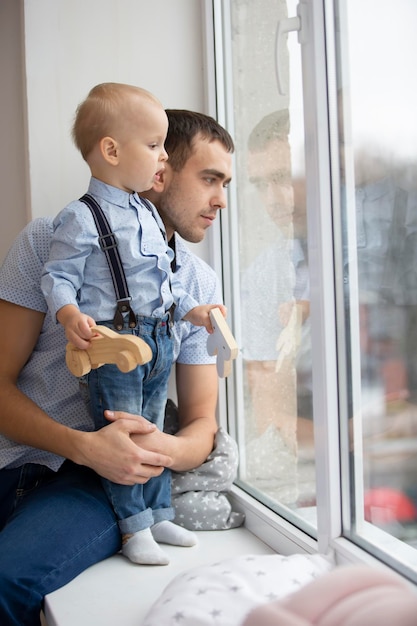Padre e hijo miran por la ventana Un hombre juega con un niño