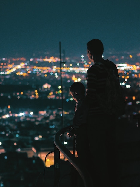 Foto padre e hijo mirando la ciudad de noche.