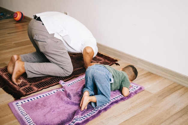 Padre e hijo musulmanes asiáticos rezando jamaah juntos en casa