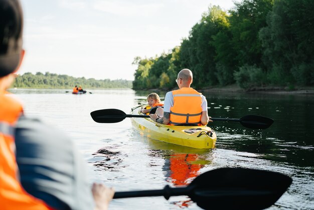 Padre e hijo en naranja chalecos salvavidas en kayak en un gran río ancho