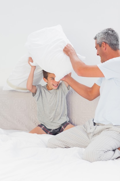 Padre e hijo peleando con almohadas en la cama en casa