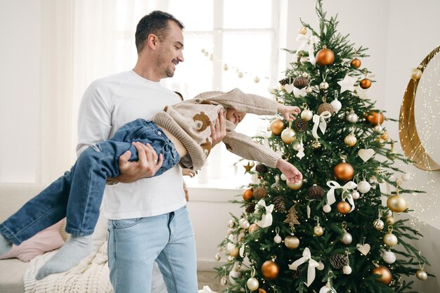 Padre e hijo pequeño divirtiéndose cerca del árbol de Navidad en casa