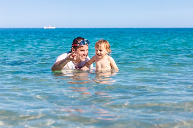 Padre e hijo pequeño divirtiéndose nadando y jugando juntos en el agua de mar en las vacaciones de verano
