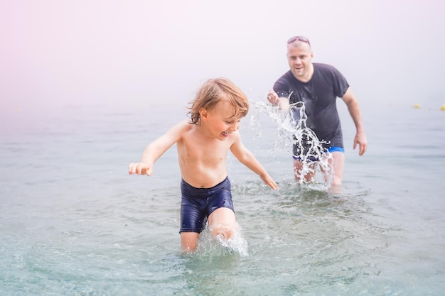 Padre e hijo pequeño jugando en el mar en un clima nublado y brumoso Papá alcanzando a su hijo en el concepto de vacaciones de verano en el agua