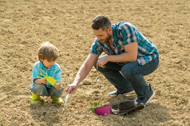 Padre e hijo plantando plantas en crecimiento jardín de primavera papá enseñando a su hijo pequeño a cuidar las plantas cavar y pala