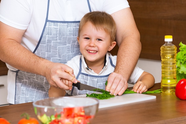 Padre e hijo preparando ensalada en la cocina con verduras