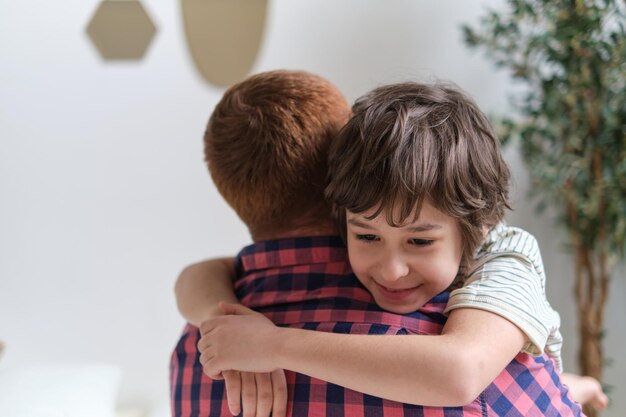 Padre e hijo regocijándose en un cálido abrazo colocados en un sofá de la sala familiar sonriendo al fotógrafo El valor de fortalecer los lazos familiares y el tiempo significativo juntos