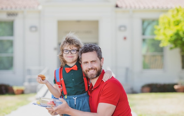 Foto padre e hijo regresan de la escuela colegial comiendo un delicioso almuerzo al aire libre