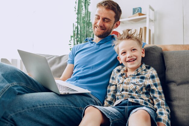 Padre e hijo sentados en el sofá y mirando algo en la computadora portátil