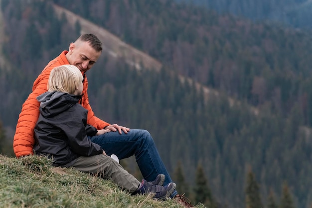 Padre e hijo se sientan en la ladera en el fondo del bosque Caminata de fin de semana en las montañas Senderismo y caminatas con niños
