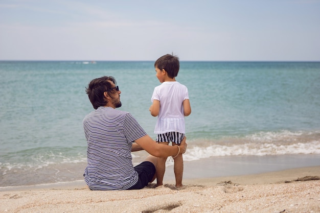 Padre e hijo se sientan en la playa con arena en el verano durante las vacaciones