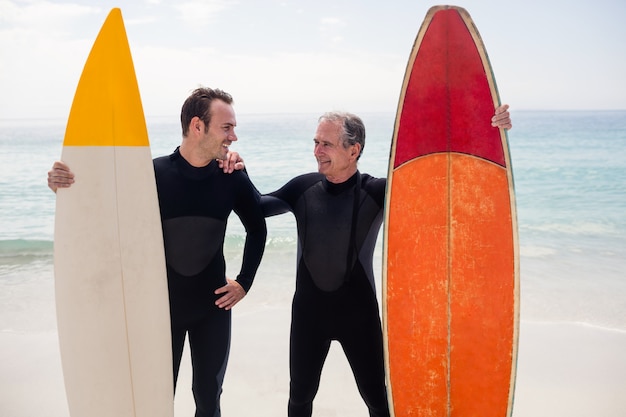 Padre e hijo con tabla de surf de pie en la playa