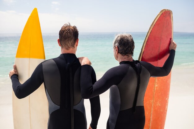 Padre e hijo con tabla de surf de pie en la playa