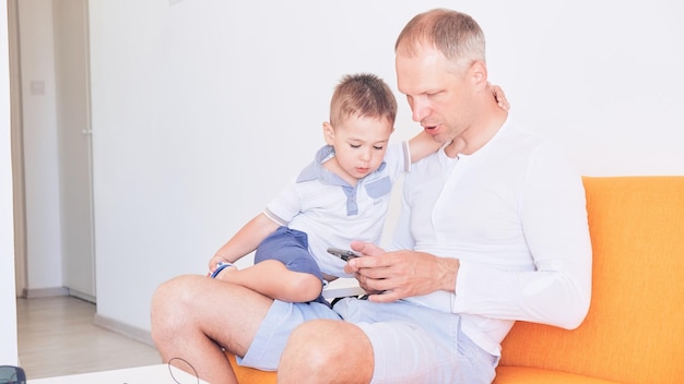 Padre e hijo usan teléfonos inteligentes y sonríen mientras pasan tiempo juntos en casa