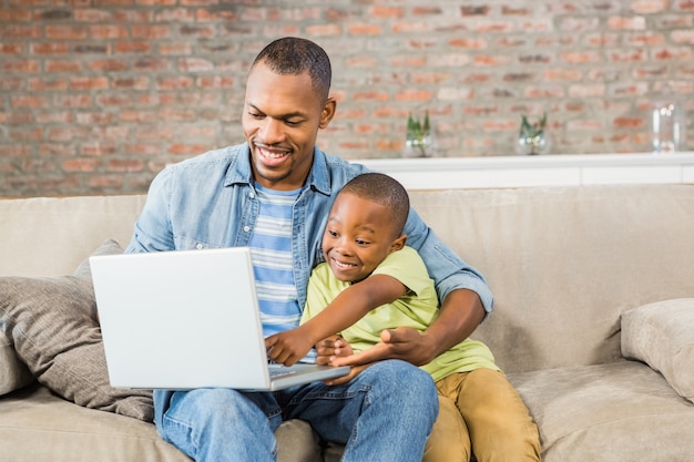 Padre e hijo usando la computadora portátil en el sofá