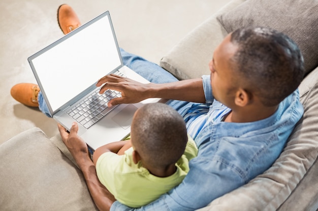 Padre e hijo usando la computadora portátil en el sofá