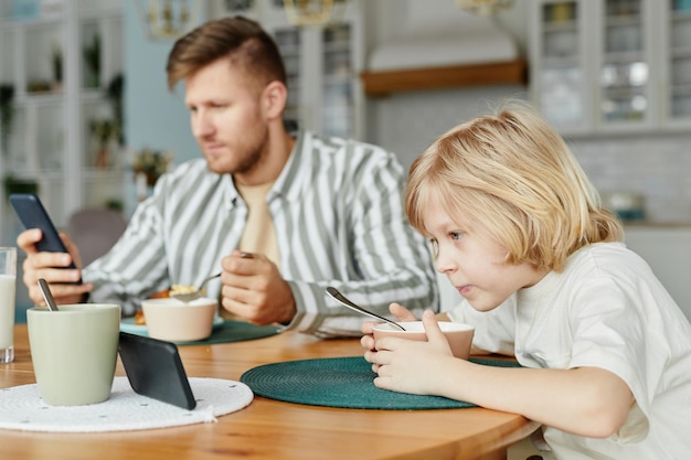 Padre e hijo usando teléfonos en el desayuno