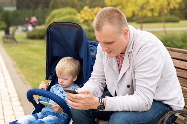 Padre e hijo usando teléfonos inteligentes mientras pasan tiempo juntos en el parque otoño.