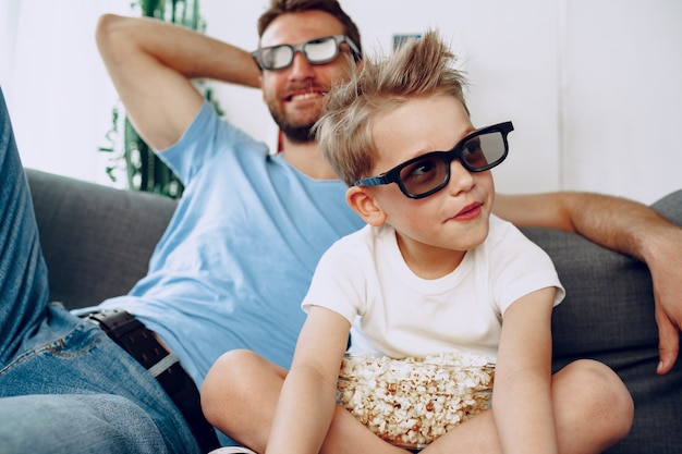 Foto padre e hijo viendo películas en casa con gafas 3d y comiendo palomitas de maíz