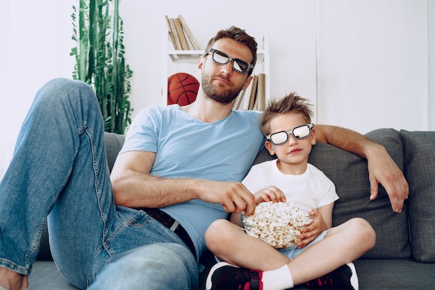 Padre e hijo viendo películas en casa con gafas 3d y comiendo palomitas de maíz