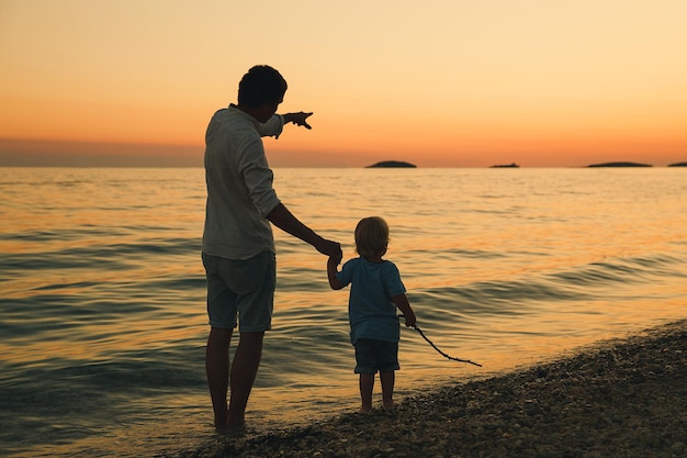 Padre e hijo vuelven siluetas caminando junto al mar Hombre y niño jugando juntos al aire libre en una playa de mar Familia amorosa y vacaciones de verano