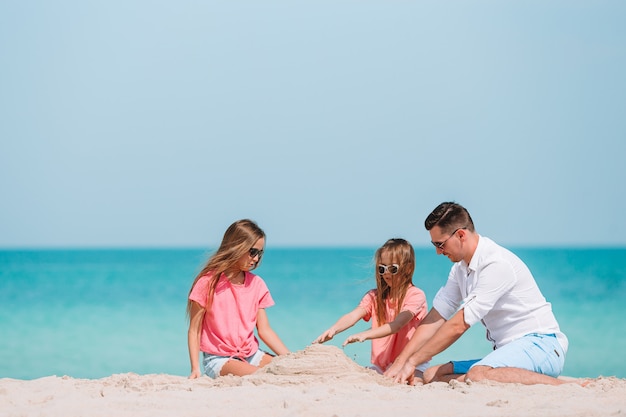 Padre e hijos haciendo castillos de arena en la playa tropical. Familia jugando con juguetes de playa