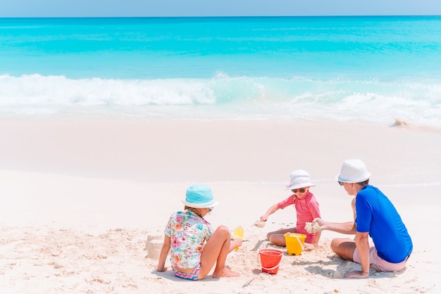 Padre e hijos haciendo castillos de arena en la playa tropical. Familia jugando con juguetes de playa